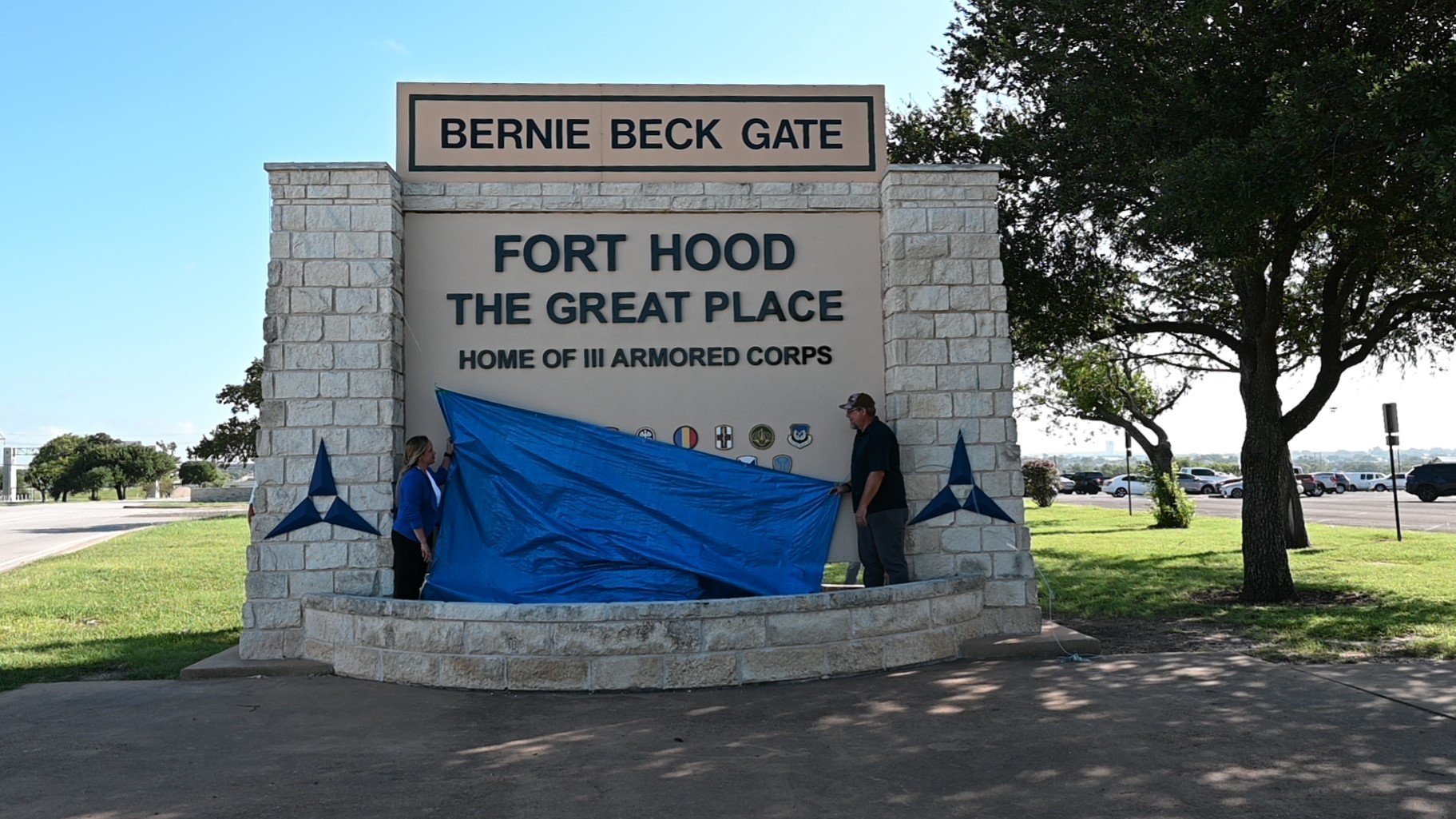 Two workers pull a tarp off the Bernie Beck Gate sign to reveal the name Fort Hood during the July 2025 renaming ceremony